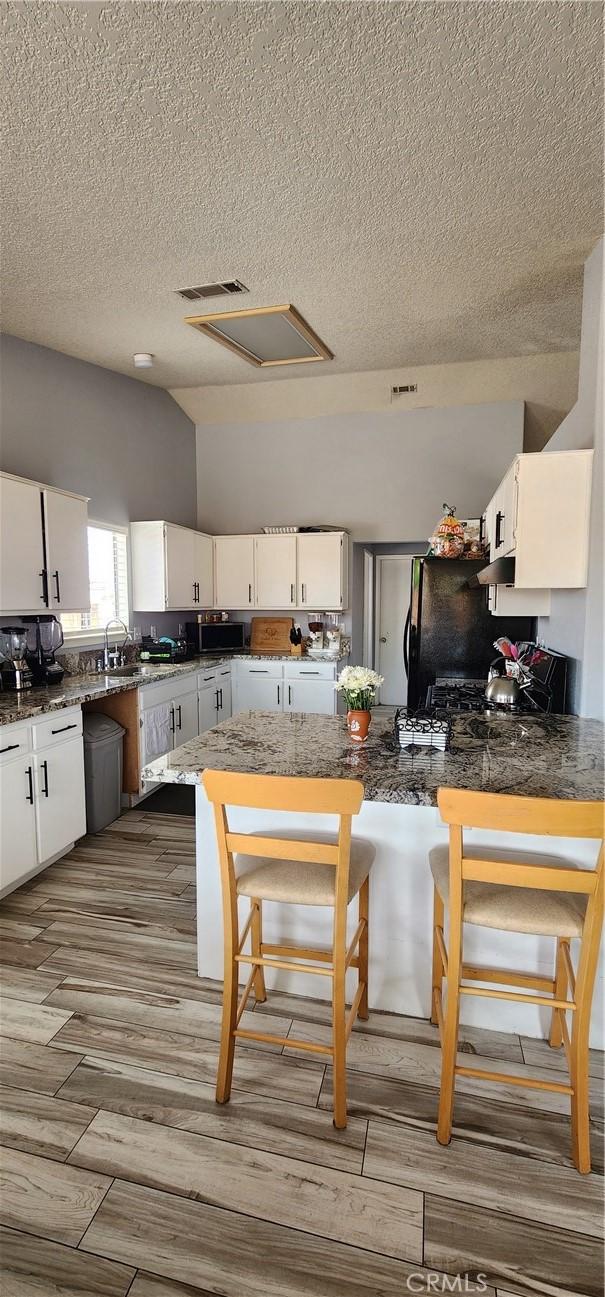 15009 Hopland St, Victorville, CA 92394 - kitchen with white cabinetry, a textured ceiling, a peninsula, wood finished floors, and a sink