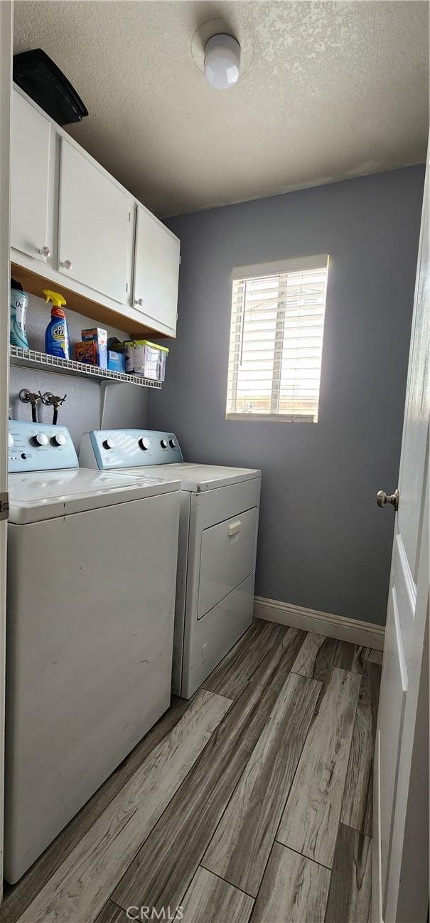 15009 Hopland St, Victorville, CA 92394 - laundry area with cabinet space, independent washer and dryer, light wood-type flooring, a textured ceiling, and baseboards