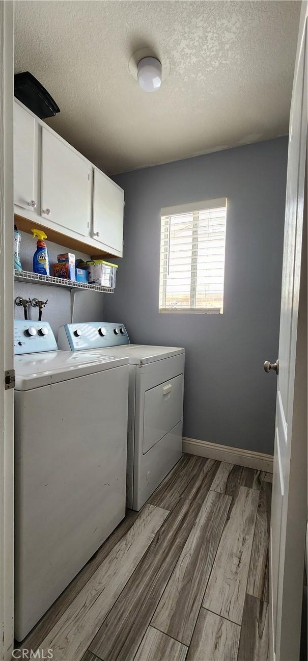 15009 Hopland St, Victorville, CA 92394 - laundry area with cabinet space, washer and clothes dryer, light wood-style flooring, a textured ceiling, and baseboards