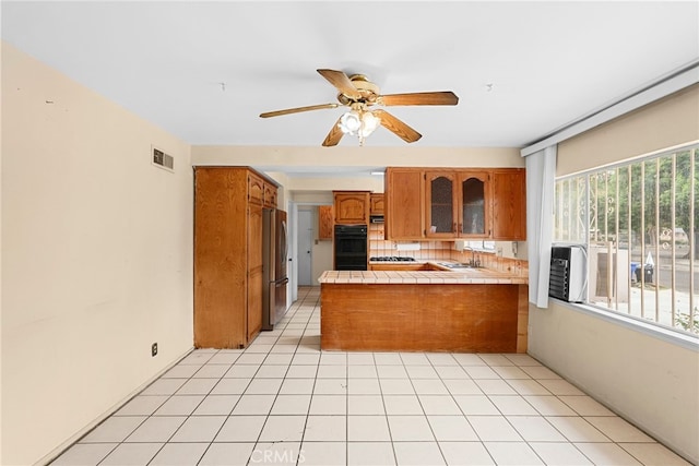 10120 Andasol Ave, Northridge, CA 91325 - kitchen with a peninsula, tile counters, brown cabinetry, freestanding refrigerator, and a ceiling fan
