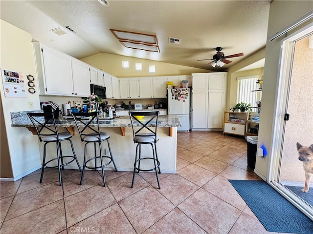 8925 Fallbrook Ct, Hesperia, CA 92344 - kitchen featuring freestanding refrigerator, a peninsula, black microwave, vaulted ceiling, and light stone countertops