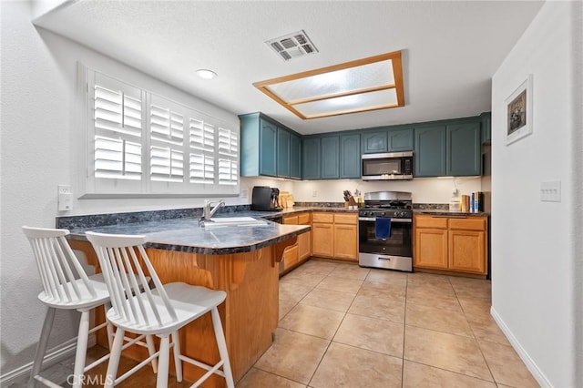 57146 Selecta Ave, Yucca Valley, CA 92284 - kitchen featuring stainless steel appliances, a sink, a peninsula, dark countertops, and a kitchen bar