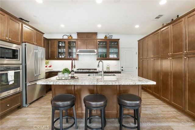 112 Cerrero Ct, Rancho Mission Viejo, CA 92694 - kitchen with stainless steel appliances, under cabinet range hood, light wood-style floors, a breakfast bar area, and tasteful backsplash