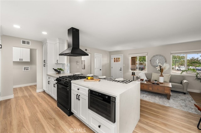 1905 Davis St, Corona, CA 92882 - kitchen with black range with gas cooktop, island exhaust hood, white cabinets, light wood-type flooring, and baseboards