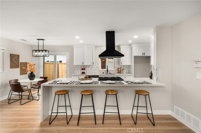 1905 Davis St, Corona, CA 92882 - kitchen featuring wall chimney range hood, a breakfast bar area, white cabinetry, decorative backsplash, and recessed lighting