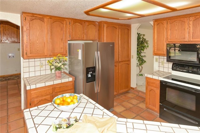 22478 Poppy Rd, Apple Valley, CA 92308 - kitchen featuring black microwave, electric stove, tile counters, stainless steel refrigerator with ice dispenser, and tasteful backsplash