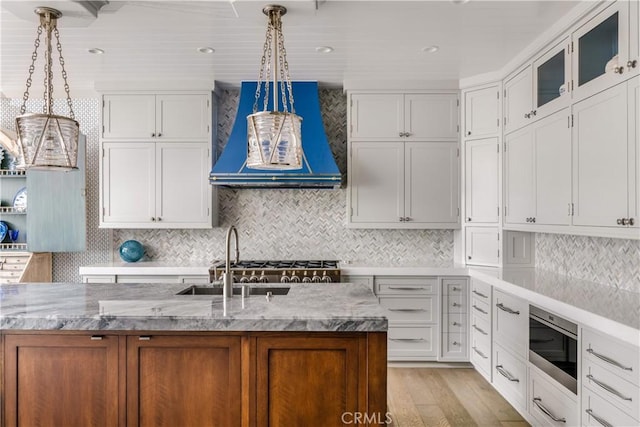 505 W Edgewater Ave, Newport Beach, CA 92661 - kitchen featuring built in microwave, wall chimney range hood, light wood-style flooring, pendant lighting, and light stone counters