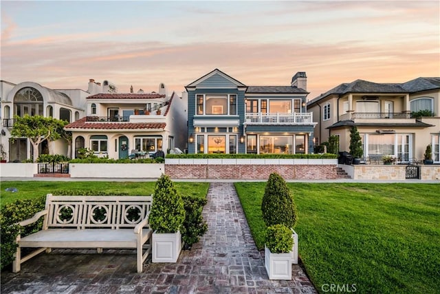 505 W Edgewater Ave, Newport Beach, CA 92661 - back of house at dusk featuring a balcony, a lawn, and a chimney