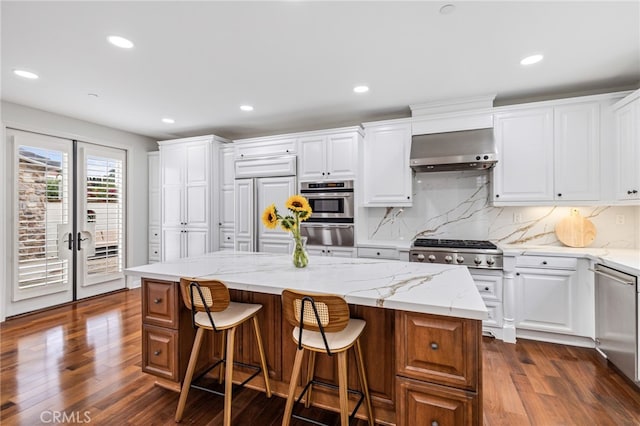 12 John, Ladera Ranch, CA 92694 - kitchen with wall chimney range hood, a warming drawer, stainless steel appliances, dark wood finished floors, and white cabinets