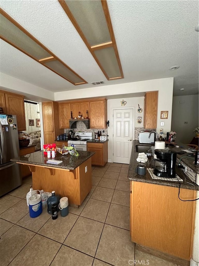 1612 Via Colabria, Gustine, CA 95322 - kitchen featuring freestanding refrigerator, white gas range, a center island, light tile patterned floors, and brown cabinetry