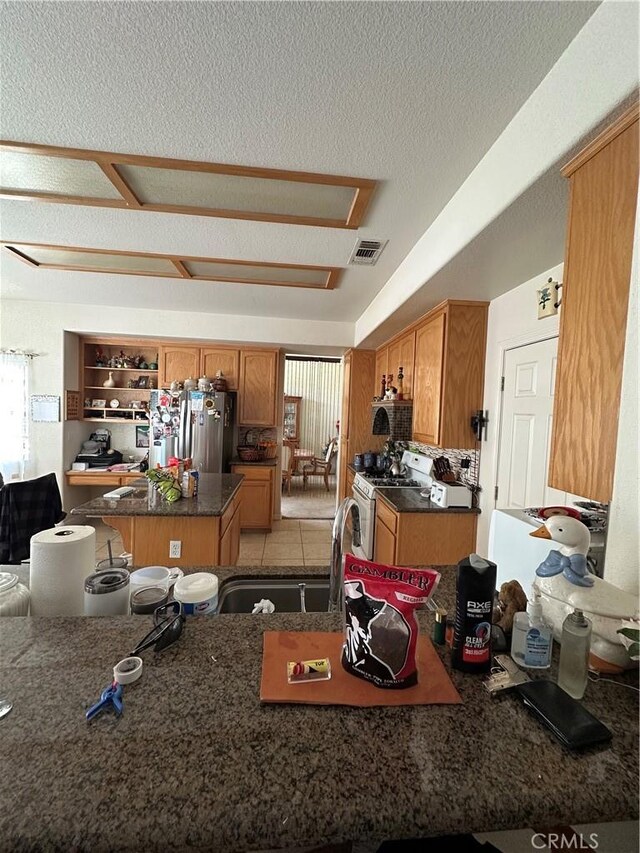 1612 Via Colabria, Gustine, CA 95322 - kitchen featuring white gas stove, freestanding refrigerator, a kitchen island, dark countertops, and a textured ceiling