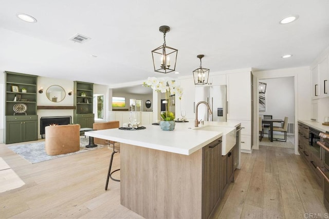 5233 Belardo Dr, San Diego, CA 92124 - kitchen featuring a lit fireplace, light wood finished floors, stainless steel fridge, a kitchen island with sink, and light countertops