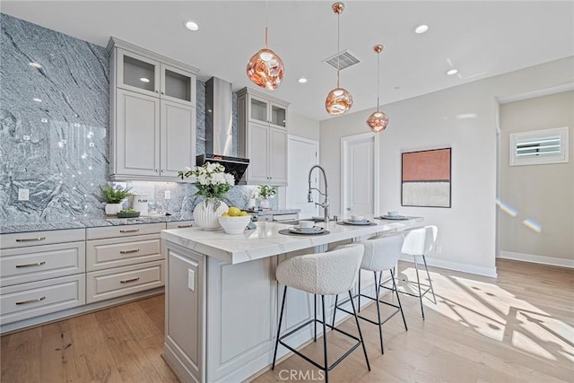 26290 Paseo Sillin, San Juan Capistrano, CA 92675 - kitchen with wall chimney exhaust hood, backsplash, a center island with sink, light wood finished floors, and a sink