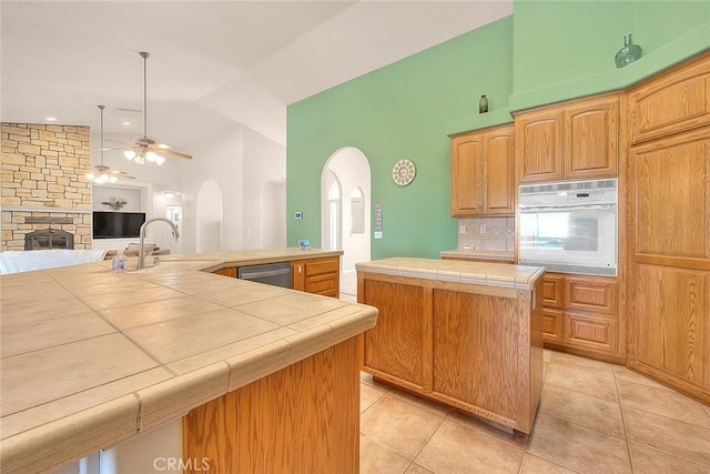 8250 Snow Cap Ave, Pinon Hills, CA 92372 - kitchen featuring white oven, tile countertops, arched walkways, a sink, and a fireplace