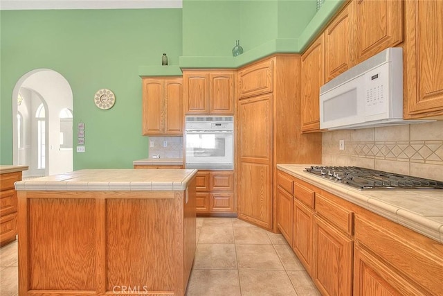 8250 Snow Cap Ave, Pinon Hills, CA 92372 - kitchen with white appliances, tile countertops, decorative backsplash, arched walkways, and a towering ceiling