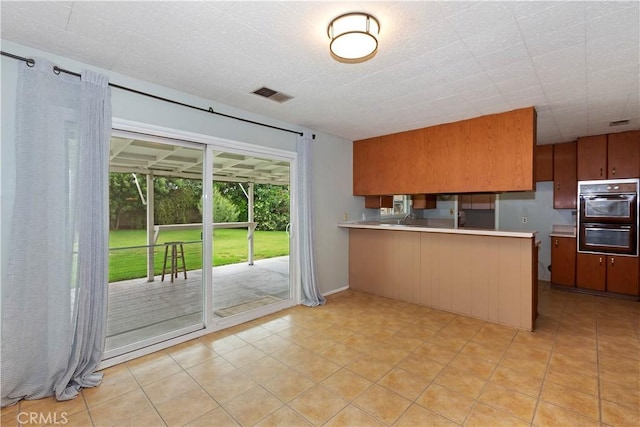 738 S Hollenbeck Ave, Covina, CA 91723 - kitchen with light countertops, a peninsula, brown cabinets, and light tile patterned floors