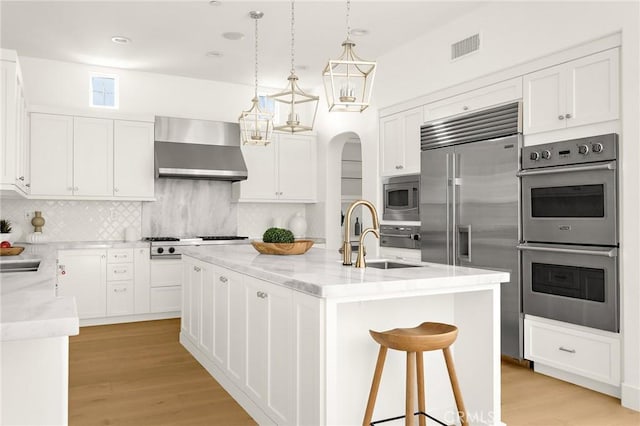 3 Seabluff, Newport Beach, CA 92660 - kitchen featuring built in appliances, wall chimney range hood, a center island with sink, and white cabinetry