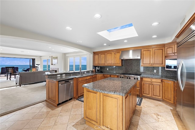 911 Buena Vis Unit 1, San Clemente, CA 92672 - kitchen featuring appliances with stainless steel finishes, wall chimney exhaust hood, a skylight, stone tile flooring, and recessed lighting
