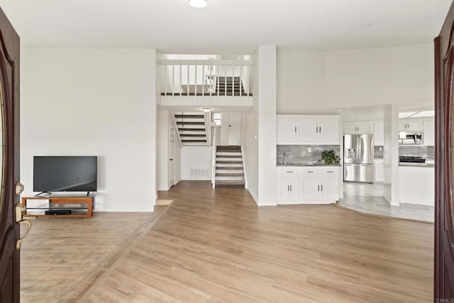1295 Buenos Ave, San Diego, CA 92110 - unfurnished living room with stairs, a high ceiling, light wood-style flooring, and baseboards