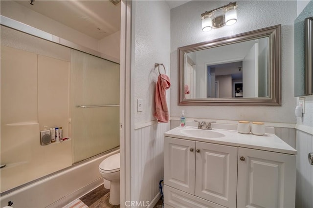 45 Stenner St Unit E, San Luis Obispo, CA 93405 - full bath with toilet, vanity, combined bath / shower with glass door, a wainscoted wall, and a textured wall