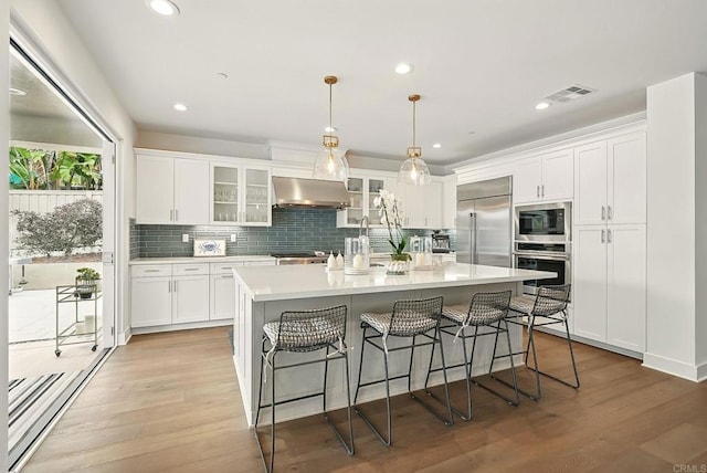 939 Moonstone Ct, Encinitas, CA 92024 - kitchen featuring ventilation hood, built in appliances, white cabinets, tasteful backsplash, and light countertops