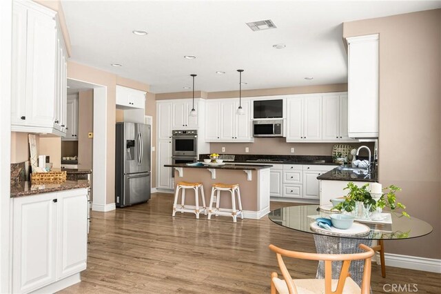 2437 N Eaton Ct, Orange, CA 92867 - kitchen with stainless steel appliances, white cabinetry, a kitchen island, a kitchen bar, and light wood-style floors