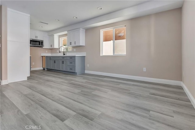 22022 Pioneer Blvd Unit A & B, Hawaiian Gardens, CA 90716 - kitchen featuring stainless steel microwave, light countertops, light wood-style flooring, gray cabinets, and white cabinetry