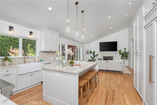 1247 Journeys End Dr, La Canada Flintridge, CA 91011 - kitchen featuring white cabinetry, lofted ceiling, light stone counters, light wood finished floors, and a center island with sink