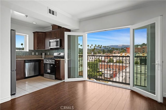 5633 Carlton Way Unit 503, Hollywood, CA 90028 - kitchen with stainless steel appliances, dark brown cabinets, decorative backsplash, light wood-style floors, and crown molding