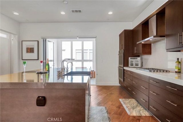 5823 Seahorse Ct, Playa Vista, CA 90094 - kitchen with wall chimney range hood, stainless steel appliances, wood finished floors, light countertops, and dark brown cabinetry