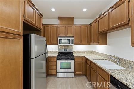4304 Owens St Unit 102, Corona, CA 92883 - kitchen featuring appliances with stainless steel finishes, light wood finished floors, brown cabinets, light stone countertops, and recessed lighting