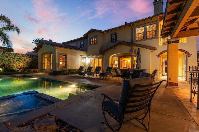 6937 Corte Langosta, Carlsbad, CA 92009 - back of house at dusk featuring a patio area, stucco siding, a chimney, and a pool with connected hot tub