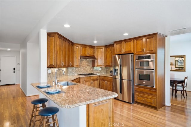 4583 Tuscani Dr, Cypress, CA 90630 - kitchen featuring appliances with stainless steel finishes, a sink, a peninsula, brown cabinetry, and light wood-type flooring
