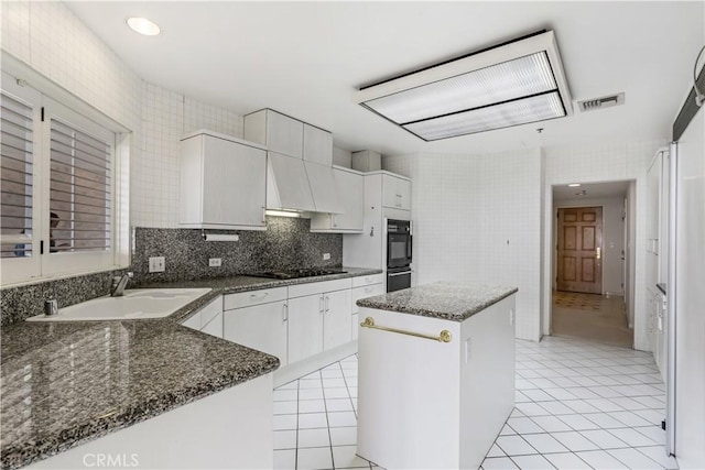 10724 Wilshire Blvd Unit 1010, Los Angeles, CA 90024 - kitchen featuring a center island, light tile patterned floors, white cabinetry, black appliances, and tile walls