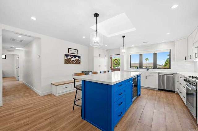 1125 Arcadia Rd, Encinitas, CA 92024 - kitchen with appliances with stainless steel finishes, blue cabinets, white cabinets, a breakfast bar, and light wood-style flooring