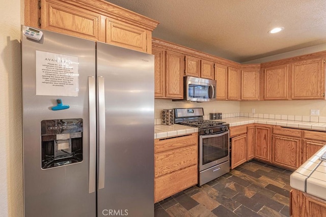 42756 Tannenbaum Platz, Big Bear Lake, CA 92315 - kitchen featuring appliances with stainless steel finishes, tile counters, recessed lighting, stone finish flooring, and a textured ceiling