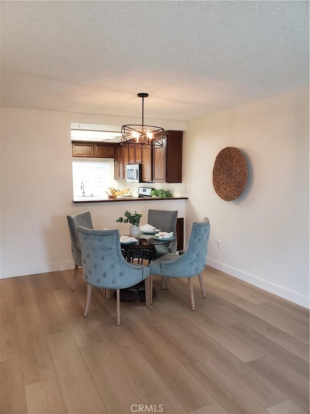 1406 Brett Pl Unit 112, San Pedro, CA 90732 - dining room featuring light wood-style flooring, a chandelier, a textured ceiling, and baseboards