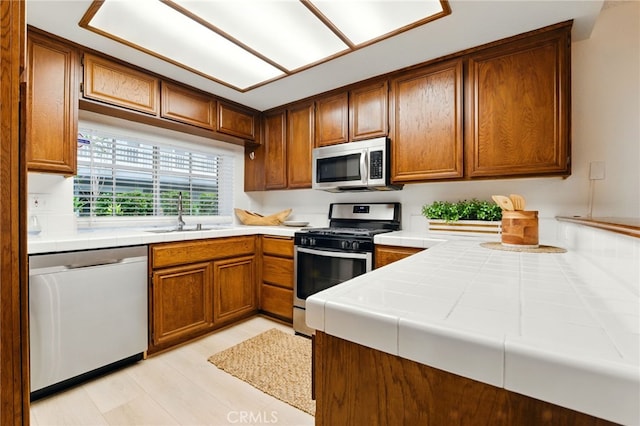 1406 Brett Pl Unit 112, San Pedro, CA 90732 - kitchen with stainless steel appliances, tile countertops, brown cabinetry, and light wood-type flooring