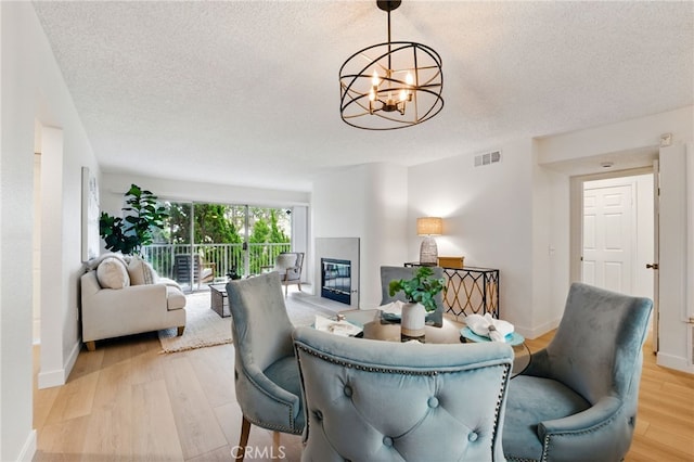 1406 Brett Pl Unit 112, San Pedro, CA 90732 - dining area featuring a chandelier, light wood-style flooring, a textured ceiling, and a glass covered fireplace