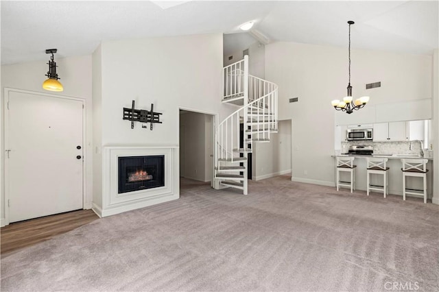 26904 Flo Ln Unit 456, Canyon Country, CA 91351 - unfurnished living room with high vaulted ceiling, stairway, a chandelier, light colored carpet, and a lit fireplace