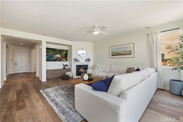 8581 Camino Limon Rd, Corona, CA 92883 - living room with light wood-type flooring, ceiling fan, a warm lit fireplace, and baseboards