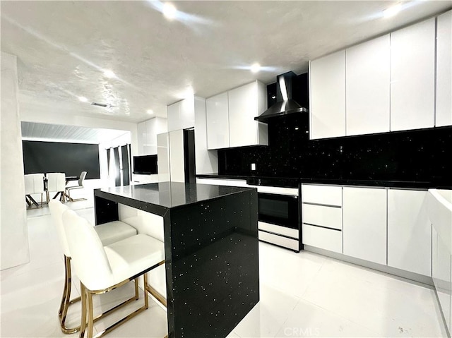 7401 Liberty Ave, Corona, CA 92881 - kitchen featuring wall chimney range hood, white cabinets, backsplash, dark countertops, and a kitchen bar