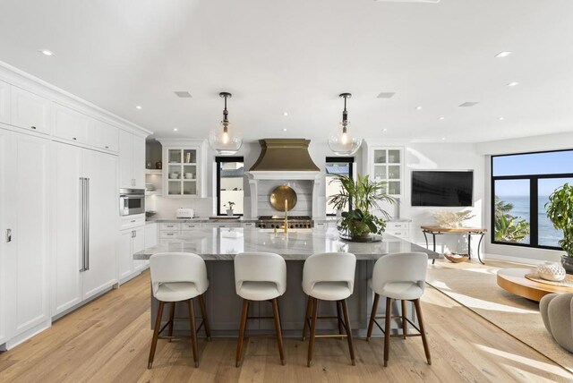 5067 Shore Dr, Carlsbad, CA 92008 - kitchen featuring light wood finished floors, white cabinetry, a large island with sink, glass insert cabinets, and recessed lighting