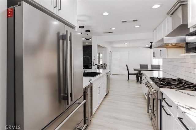 1222 W Kettering St, Lancaster, CA 93534 - kitchen with high quality appliances, wall chimney exhaust hood, backsplash, light wood-style floors, and recessed lighting