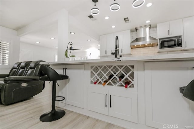 1222 W Kettering St, Lancaster, CA 93534 - kitchen featuring wall chimney exhaust hood, black microwave, a breakfast bar, light wood-style floors, and white cabinetry