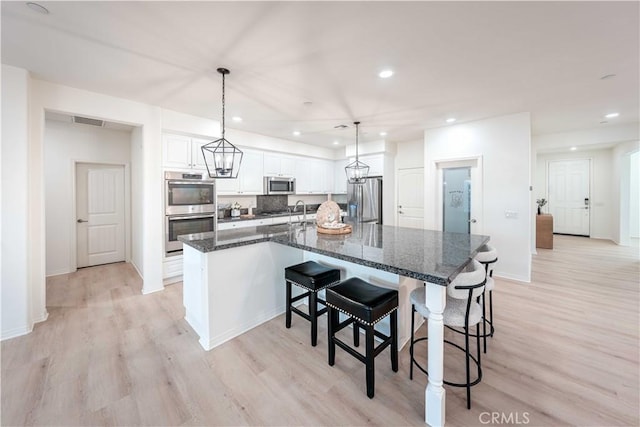 6940 Lagoon Ct, Jurupa Valley, CA 91752 - kitchen featuring stainless steel appliances, a large island with sink, light wood finished floors, white cabinets, and recessed lighting