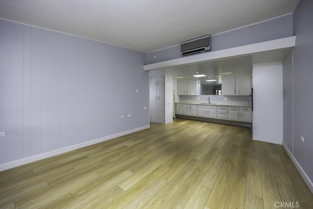 13881 Thunderbird Dr Unit M1-63E, Seal Beach, CA 90740 - unfurnished living room with a sink, light wood-style flooring, a wall mounted AC, and baseboards
