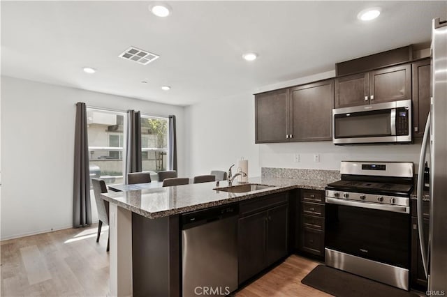 7155 Citrus Ave Unit 320, Fontana, CA 92336 - kitchen featuring appliances with stainless steel finishes, dark brown cabinets, a peninsula, light stone counters, and light wood finished floors