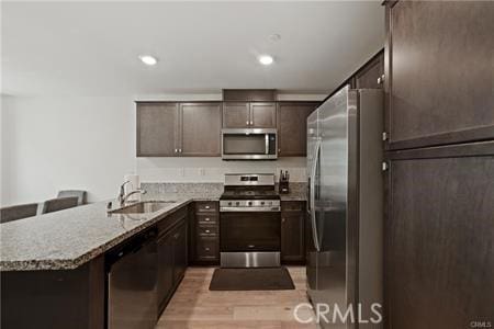 7155 Citrus Ave Unit 320, Fontana, CA 92336 - kitchen featuring stainless steel appliances, dark brown cabinets, light stone countertops, a peninsula, and light wood-type flooring