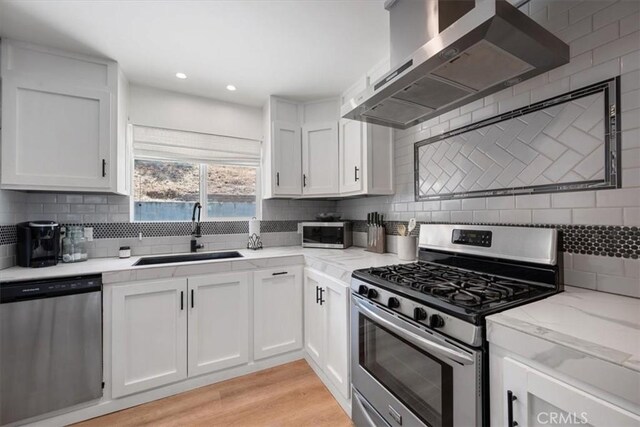 7560 Castano Ave, Atascadero, CA 93422 - kitchen featuring stainless steel appliances, wall chimney range hood, white cabinetry, decorative backsplash, and light wood-type flooring